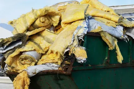 Yellow insulation rolls overflowing a green dumpster.