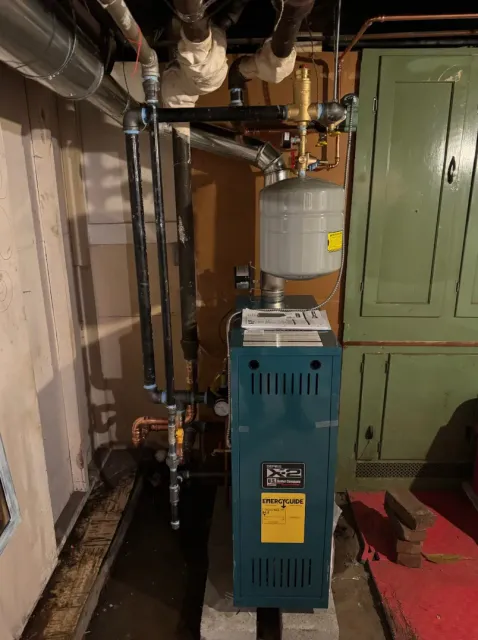 A blue and gray furnace in a basement with connected pipes and tank.