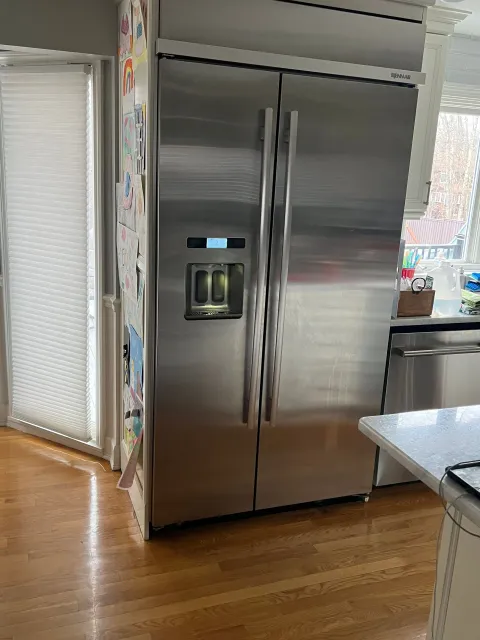 A stainless steel refrigerator is sitting in a kitchen next to a window.