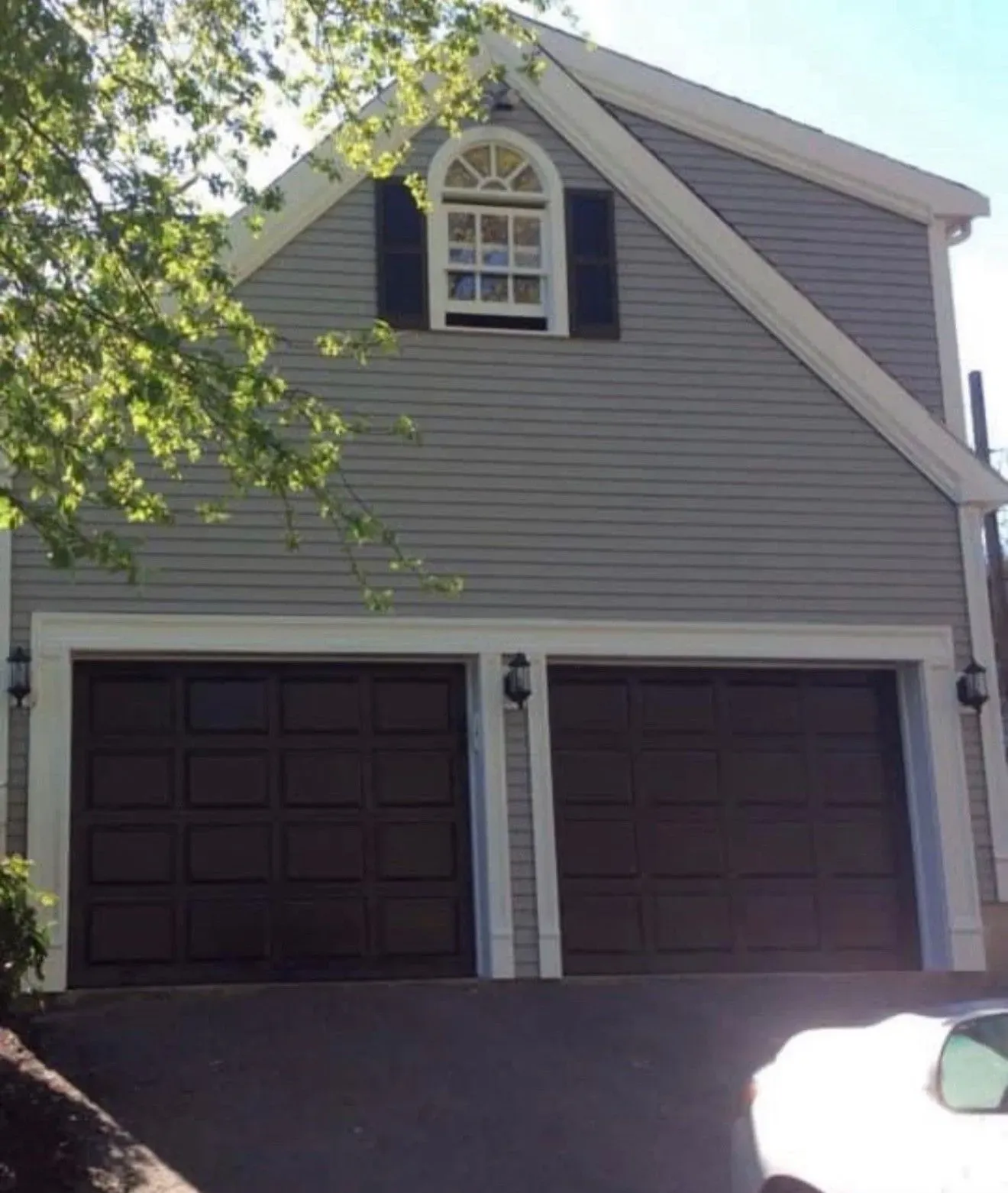 Two-story gray house with dark garage doors and a small arched window above them.
