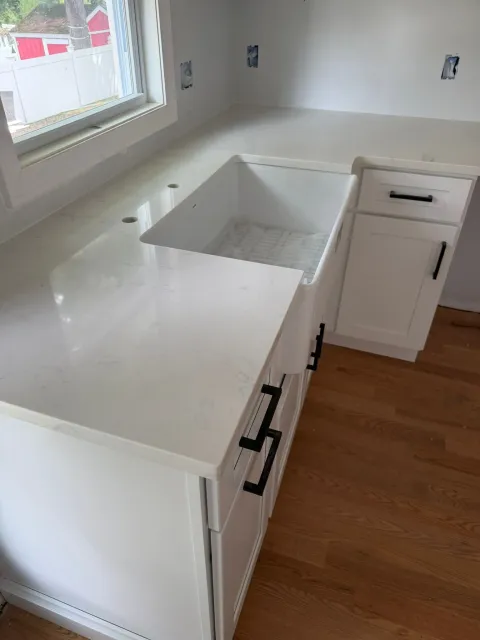 White kitchen countertop with sink cutout, black handles, and light wood floor by a window