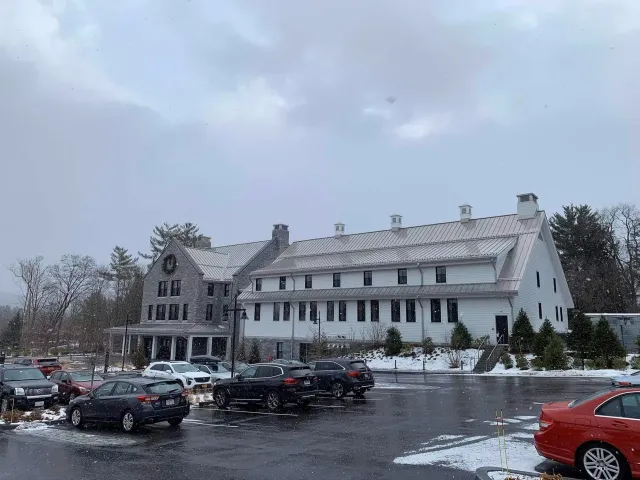 Snowy day with a two-story white building, stone facade, cars in a parking lot.