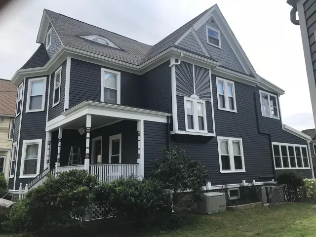 Dark blue two-story home with white trim and covered porch, freshly painted by Star Painting in Massachusetts suburban neighborhood