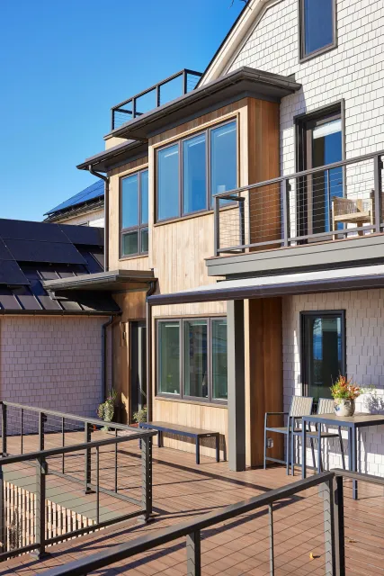 Modern residential building with large windows, wooden accents, metal railings, and a spacious wooden balcony.