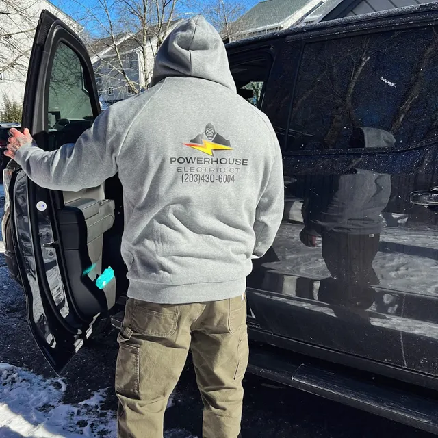Electrician Wearing a Hoodie with Powerhouse Electric Ct Logo, Standing by a Vehicle in the Snow