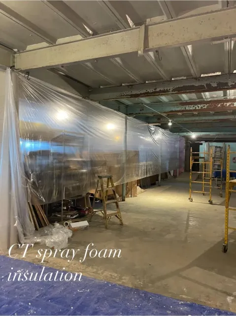 Interior of a building under construction, with a plastic barrier and exposed insulation being installed.