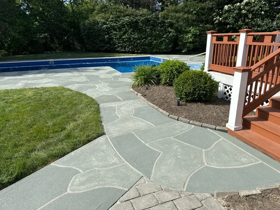 RenuKrete concrete resurfacing walkway connecting wooden deck stairs to the pool area with a slate-style finish.