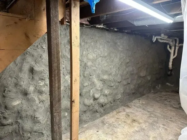 Small rough-plastered basement room with exposed ceiling beams and a fluorescent light.