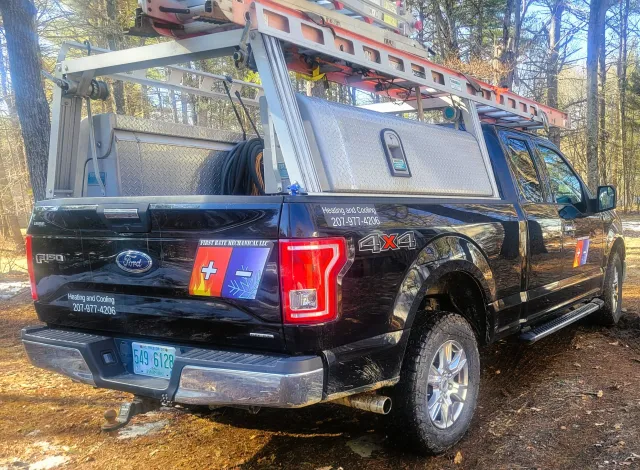 Black Ford pickup truck with ladder and equipment on top, featuring decals for heating and cooling services, a phone number, and a logo with a Swiss flag and icons for heat and cold.