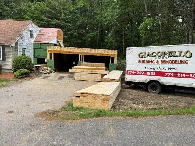 Construction site beside a house with lumber stacked near a trailer and a partially built green structure