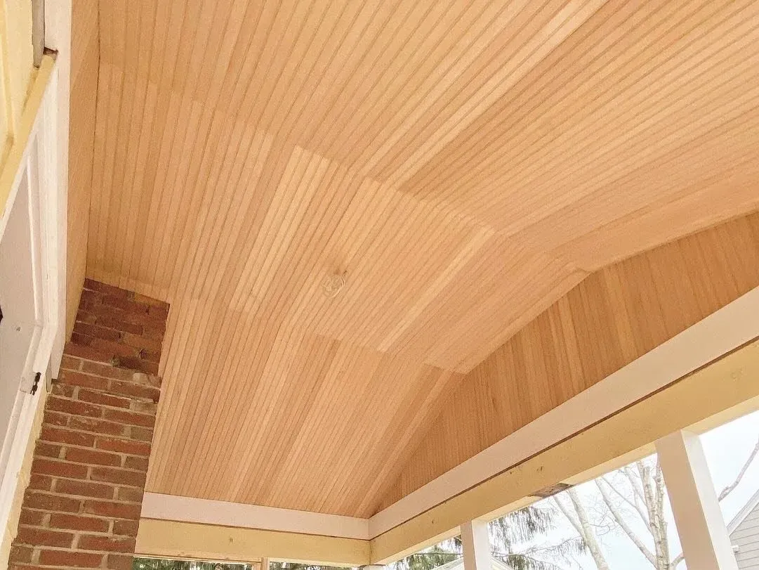 Interior view of a ceiling with wooden planks and part of a brick wall.