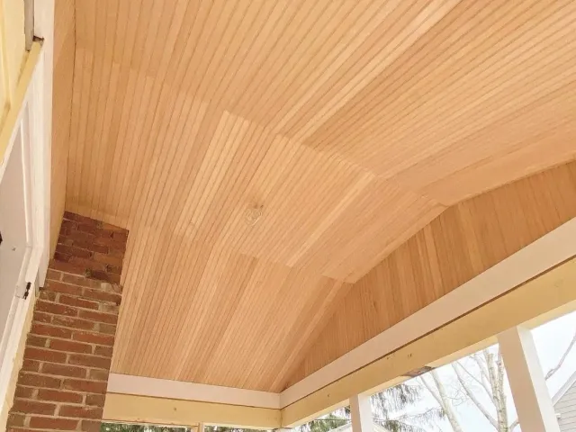 Interior view of a ceiling with wooden planks and part of a brick wall.