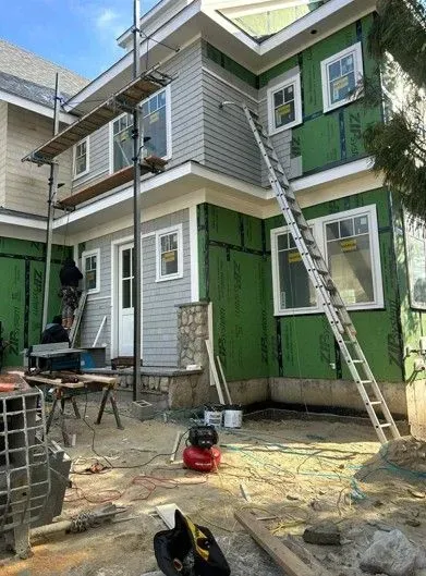 House exterior under construction with workers, ladders, scaffolding, and building materials scattered below