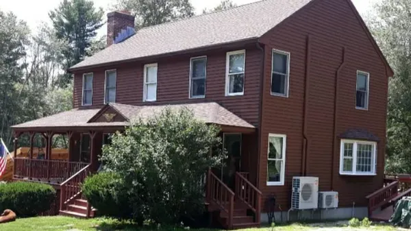 Two-story brown house with a porch. Green lawn and trees surround the home.