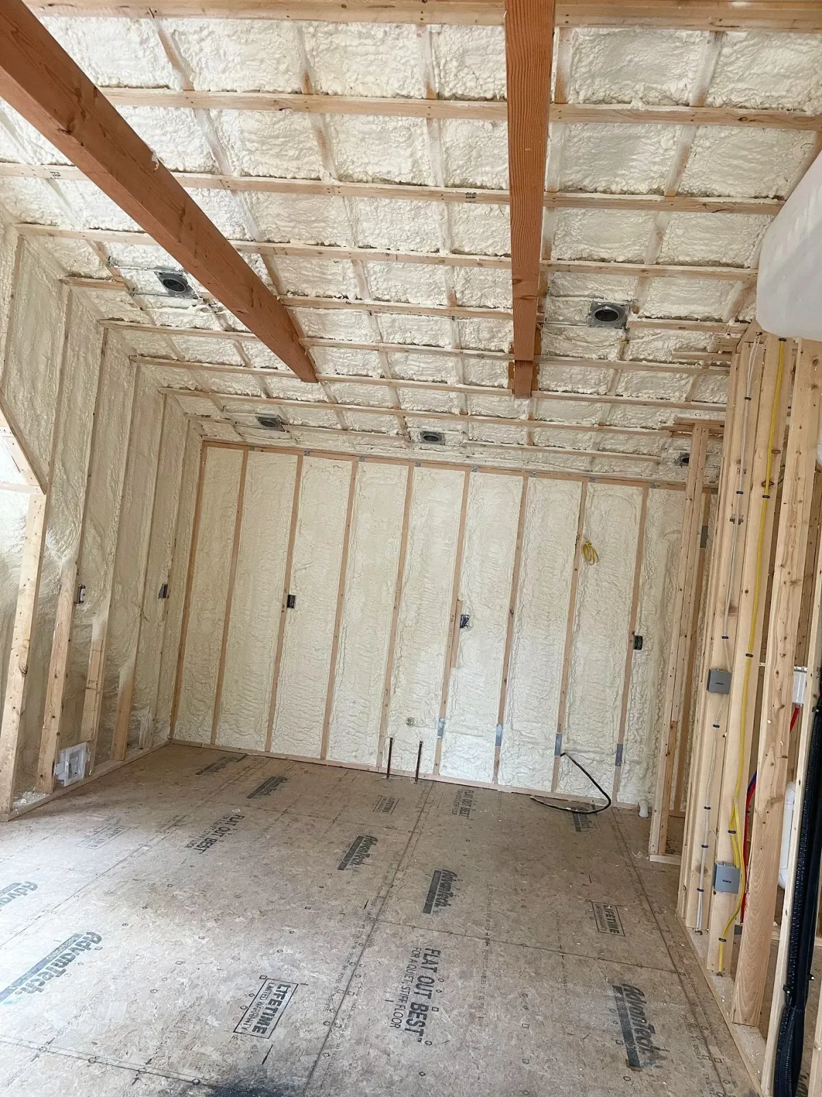Interior of a room with spray foam insulation on walls and ceiling, wooden framing.