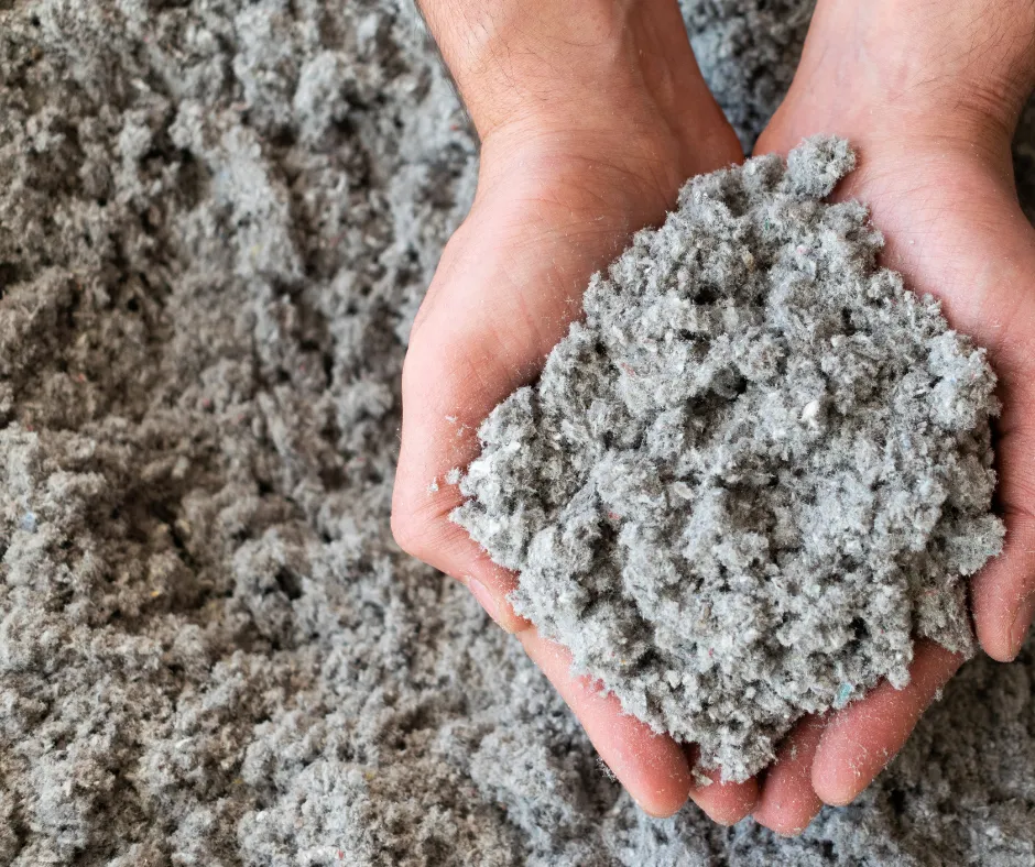 Hands holding a large clump of Cellulose insulation, recycled paper and treated for fire and pest resistance. It’s dense, effective at sealing air leaks, and ideal for attics and walls.