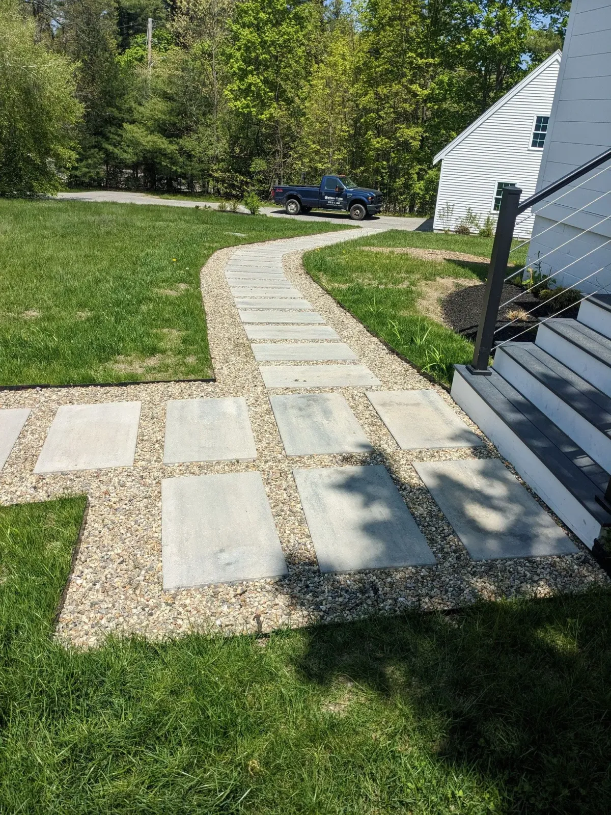 Stepping stone path through a grassy yard beside a white house, leading toward a blue car in the distance