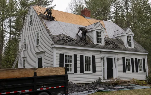 Roof replacement in progress on a New England home with old shingles torn off