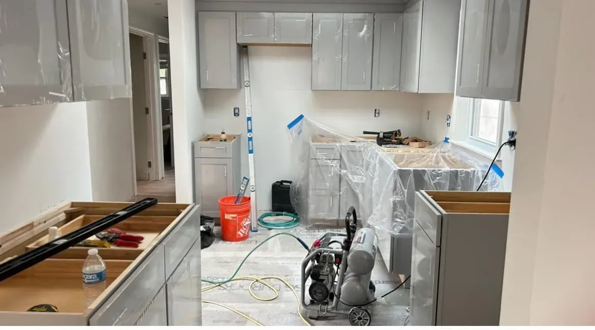A kitchen under construction with white cabinets and a bucket on the floor.