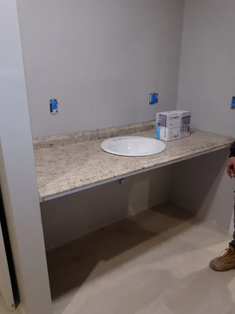 Unfinished bathroom vanity with granite countertop, white sink, exposed outlets, and a cardboard box on the counter.