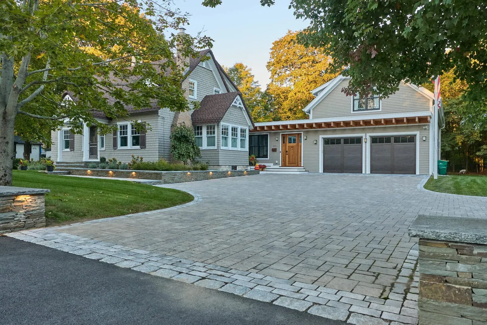 Paver driveway with tumbled cobble border, stone entrance pillars, and lit stone walls in Mansfield, MA