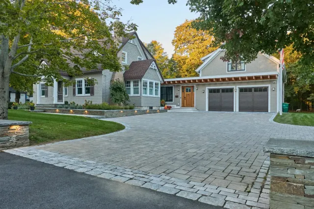 Paver driveway with tumbled cobble border, stone entrance pillars, and lit stone walls in Mansfield, MA