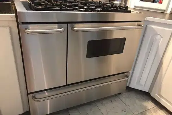 Stainless steel gas stove with a black cooktop and oven below, set between white kitchen cabinets.