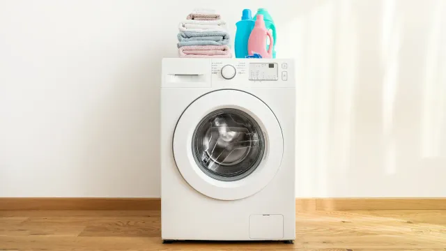 A white washing machine with a stack of clothes on top of it.