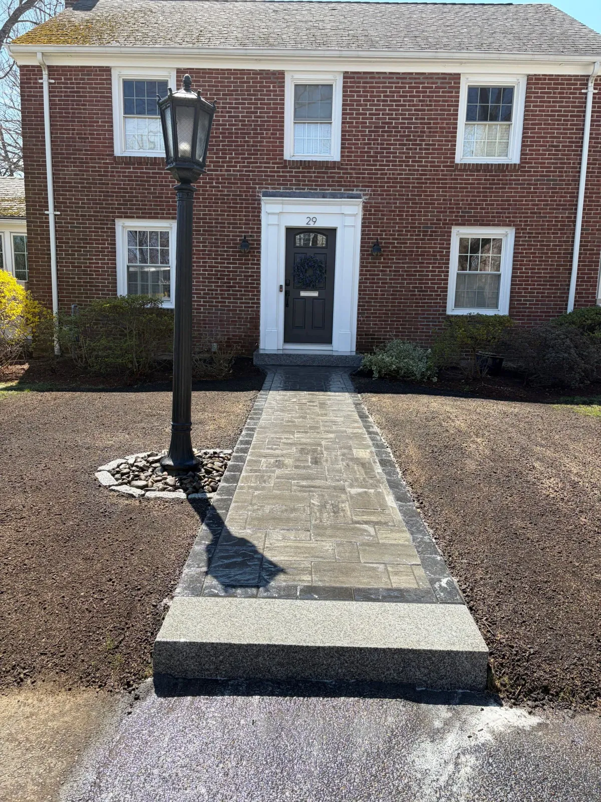 Brick building entrance with stone walkway, black lamppost, and gray front door