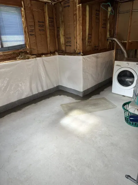 Unfinished room with exposed studs, white wall covering, concrete floor, and a washing machine on the right