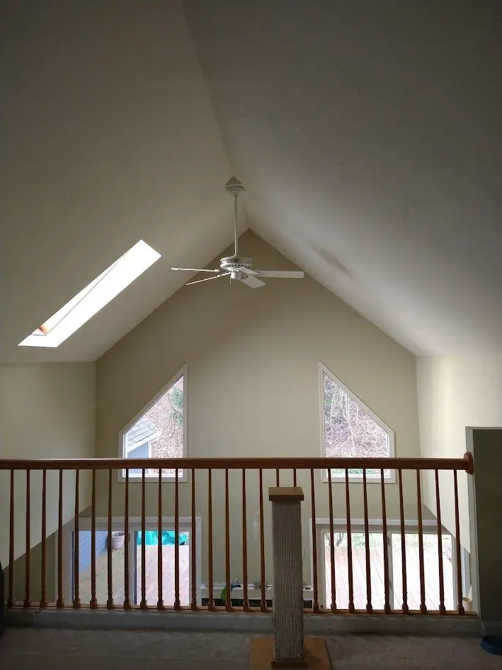 Loft interior with vaulted ceiling, ceiling fan, skylights, and railing overlooking a lower level