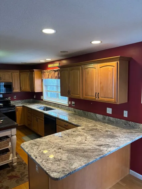 Modern kitchen with wood cabinets, granite counters, burgundy walls, and a window over the sink
