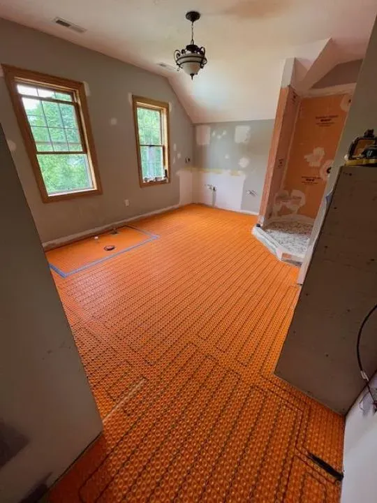 Dreamstate Renovations, LLC - Radiant heated floor installation with orange mesh underlayment in a room, showcasing the process of creating a cozy and energy-efficient living space.
