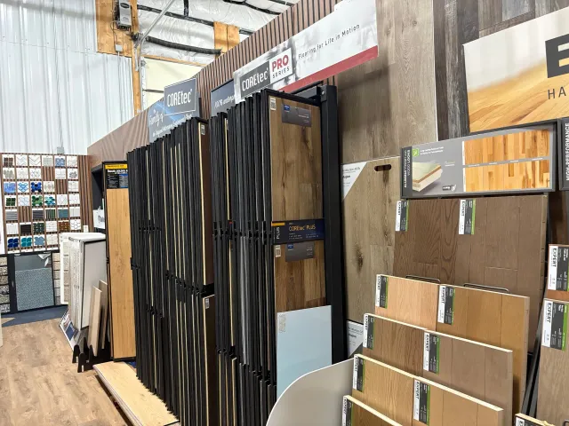 Tile and flooring showroom with sample displays and stacked wood-look panels inside a warehouse-like space