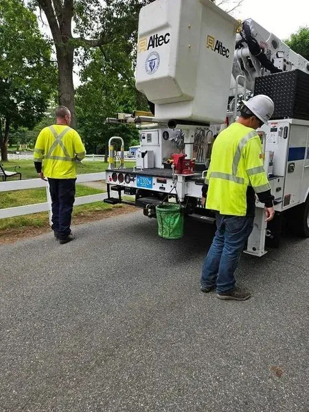 Two utility workers wearing safety vests near a bucket truck on a paved road.