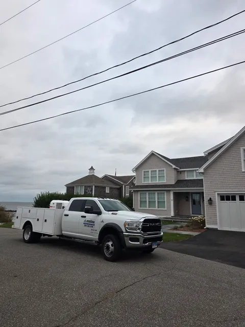 White work truck parked on a street near a house under a cloudy sky.