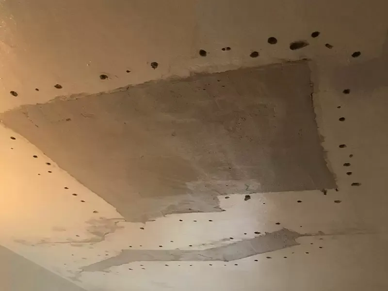 A ceiling with multiple drill holes and two patched areas where repairs have been made.