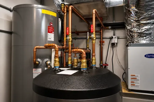 Residential boiler room with gray tanks, copper pipes, and black insulated heating equipment.