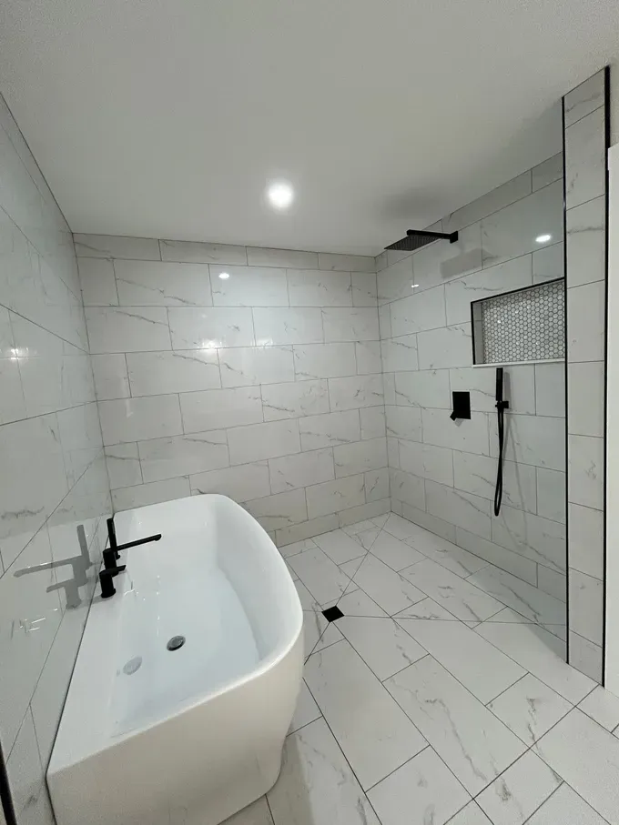 Modern white bathroom with freestanding tub, marble tile walls, and large glass shower enclosure