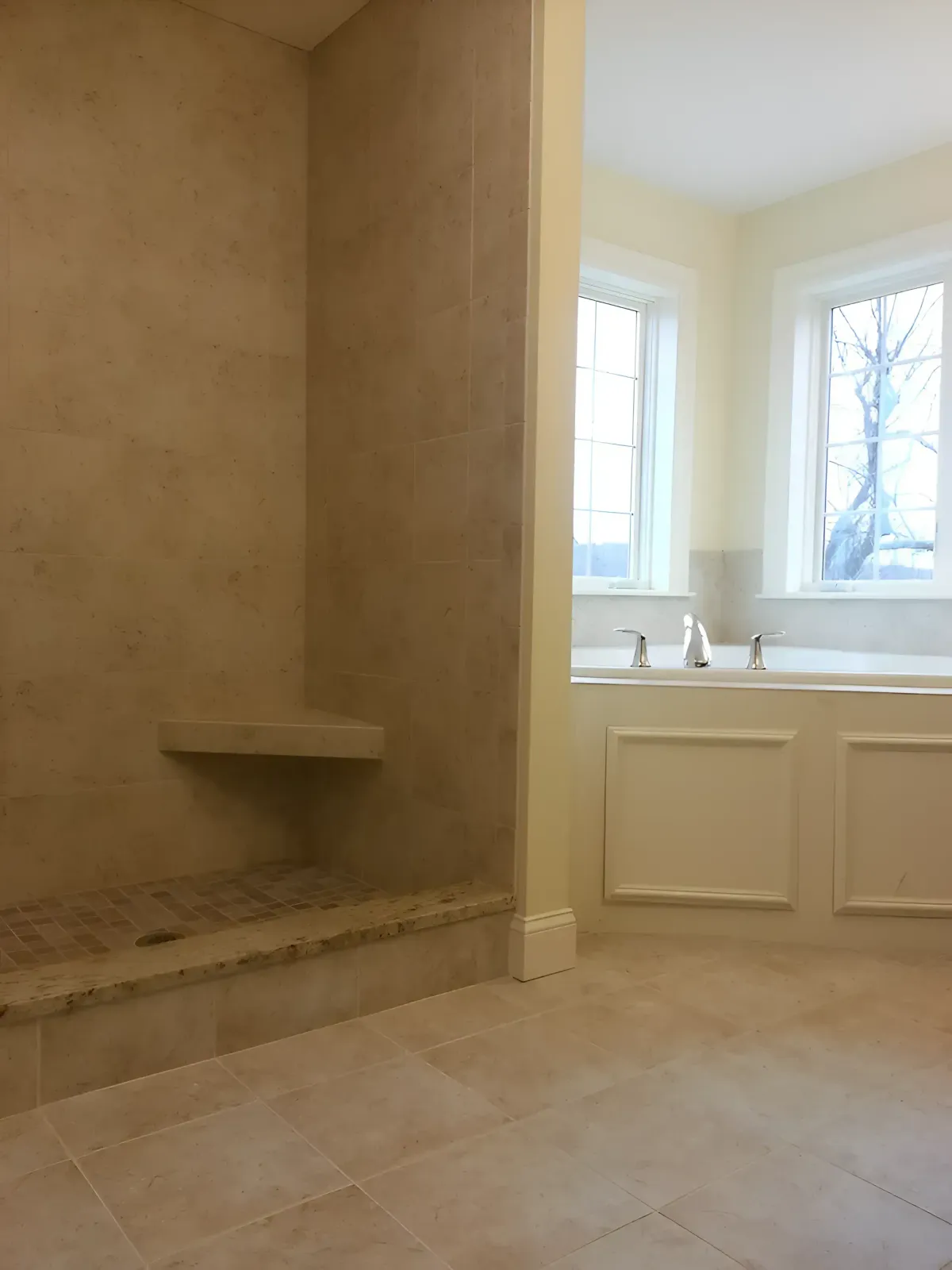 Bathroom with stone shower wall, built-in bench, and double window above a white vanity