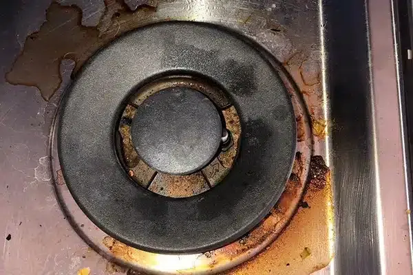 A dirty stove burner with food stains and spills on a metal surface.