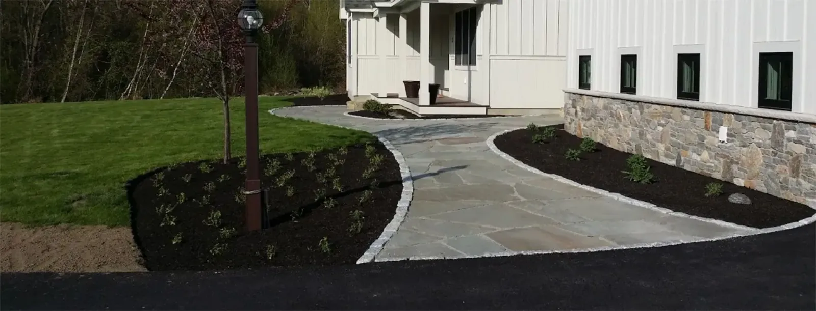 Curved stone walkway leading to a white building entrance with landscaped grass and shrubs