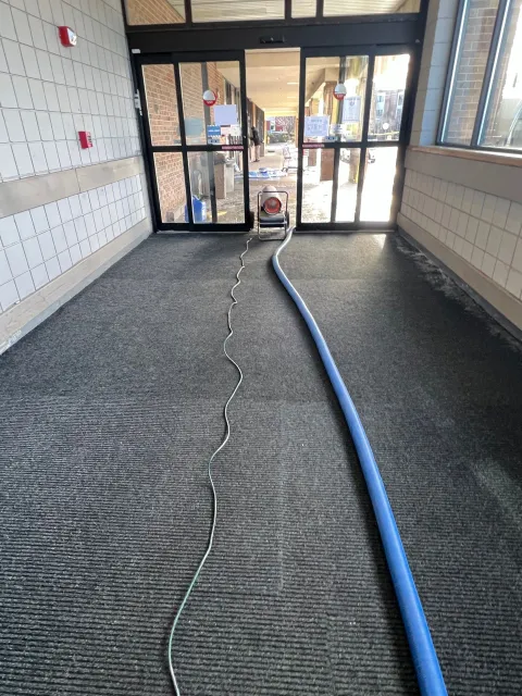 A vacuum cleaner is cleaning a carpet in a hallway.