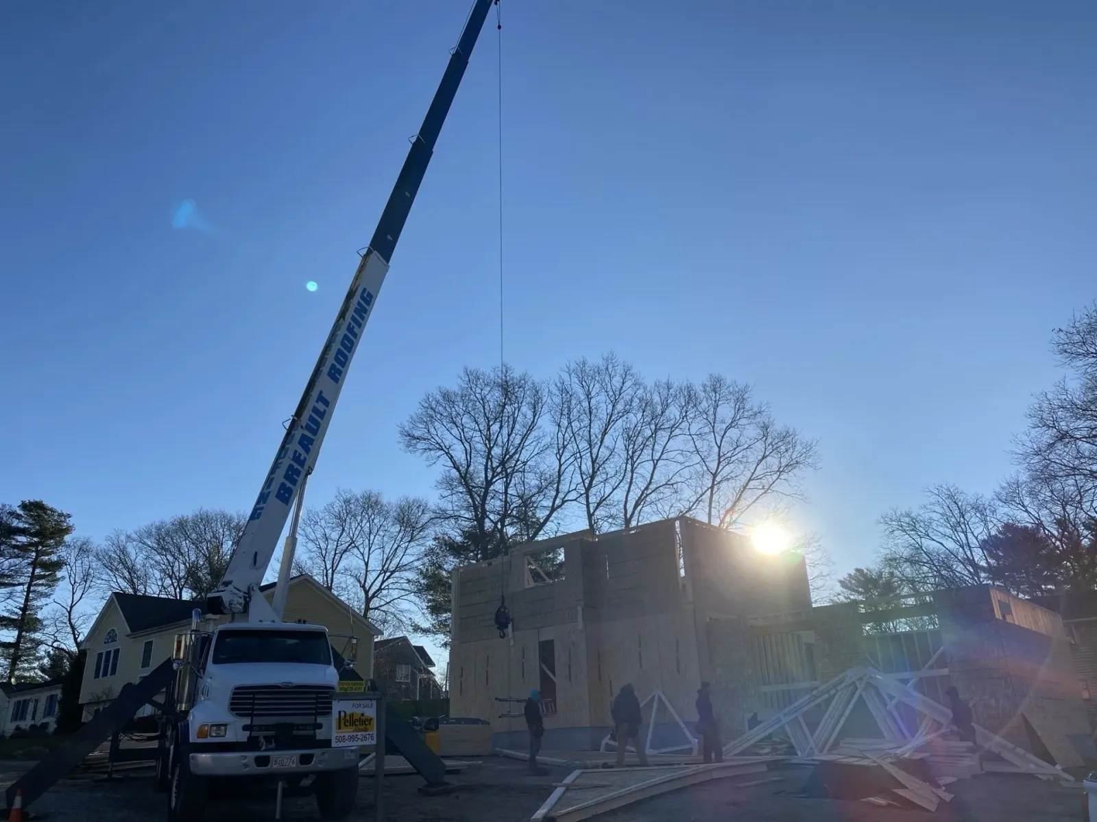 Construction site with crane lifting lumber; workers building a house on a sunny day.