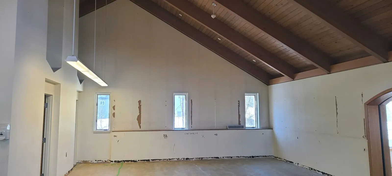 Empty attic room with white walls, exposed wooden beams, and small windows along one side