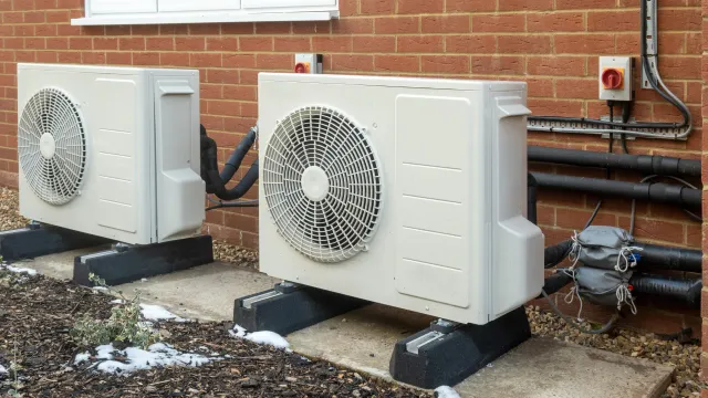 Two air conditioners are sitting outside of a brick building.