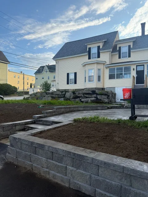 Stone steps and retaining wall leading to a cream house with a blue roof under a bright sky.