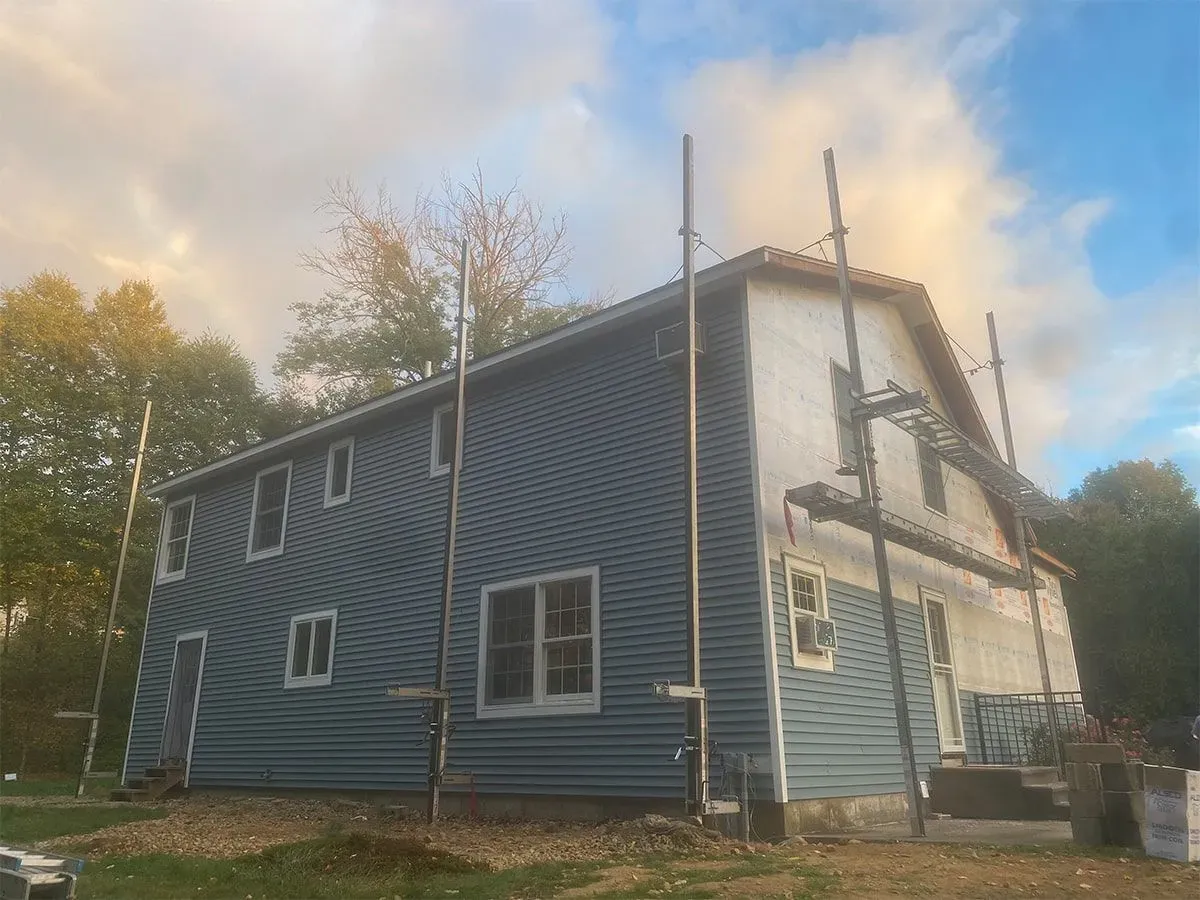 Blue house exterior with white trim, three tall poles, and trees against a cloudy sky