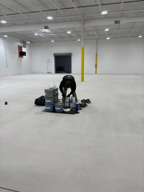 Person in a large, empty warehouse with painting supplies.