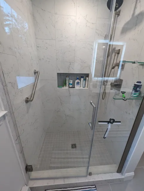 An expertly tiled standing shower in Lakeville, including grab bars, a niche, and a glass shower door.